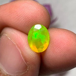 以下が含まれることがあります： 滑らかで磨かれた表面を持つ、鮮やかな緑と黄色の楕円形のオパール宝石