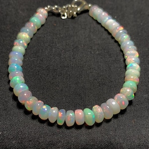 Könnte beinhalten: Ein Armband aus weißen Opalperlen mit einem silbernen Verschluss. Die Perlen sind irisierend und haben einen Regenbogen-Schimmer.
