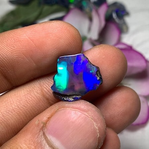 Op de afbeelding: Een ruwe opaal edelsteen in donkerblauw, groen en paars met een zwarte achterkant. De opaal is een natuurlijke steen met een unieke iriserende glans.