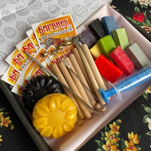 Może przedstawiać: Zestaw do zdobienia pisanek woskiem. Zestaw zawiera różne narzędzia, wosk i saszetki z barwnikiem. Saszetki z barwnikiem są oznaczone "Барвник для писанок", co oznacza "Barwnik do pisanek".