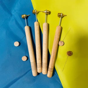 Puede incluir: Cuatro herramientas de madera con puntas de latón y líneas negras. Las herramientas están sobre una superficie azul y amarilla.