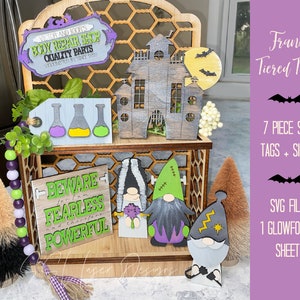 May include: A tiered tray with a Halloween theme. The tray features a wooden sign that says "Victor and Igor's Body Repair Shop Quality Parts Shocking You to Life Since 1808", a wooden sign that says "Beware I am Fearless and therefore Powerful", a wooden house, and three gnomes. The gnomes are painted in different colors and have different accessories. The tray is made of wood and has a black and white checkered pattern.