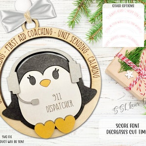 May include: A wooden Christmas ornament shaped like a penguin wearing a headset with the text "911 Dispatcher" on the front. The ornament is decorated with a white bow and the text "Chaos Controlling - First Aid Coaching - Unit Sending - Calming".