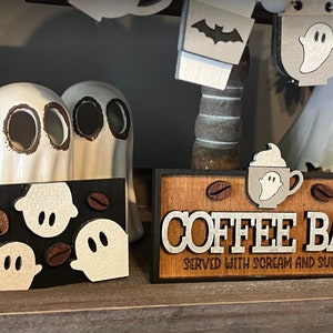 May include: A wooden sign with the text "COFFEE BAR SERVED WITH SCREAM AND SUGAR" in white letters. The sign is decorated with coffee beans and ghosts.