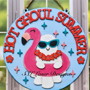 May include: Round wooden sign with the words "HOT GHOUL SUMMER" in red letters. A ghost wearing sunglasses and a flower lei floats in a pink flamingo pool float. The sign has a blue background with star and flower accents.