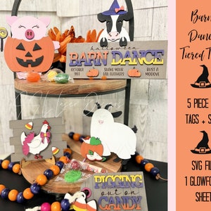 Op de afbeelding: Een vijfstukse Halloween-tiered tray set met een schuurdans thema. De set bevat een bord met de tekst "Barn Dance", een varken in een pompoenkostuum, een koe, een kip en een spook. De set is gemaakt van hout en is geschilderd in verschillende kleuren. De set is perfect om een huis voor Halloween te versieren.