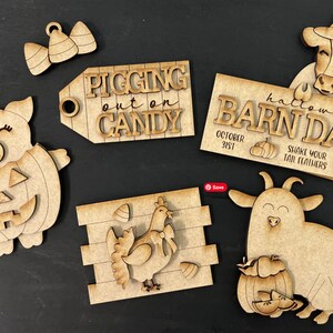 Op de afbeelding: Een set van zes houten uitsnijdingen voor een Halloween-schuurdans thema. De uitsnijdingen omvatten een varken dat een pompoenkostuum draagt, een koe die een heksenhoed draagt, een geit die een pompoen vasthoudt, een kip, een bord met de tekst "Pigging out on Candy", en een bord met de tekst "Halloween Barn Dance".