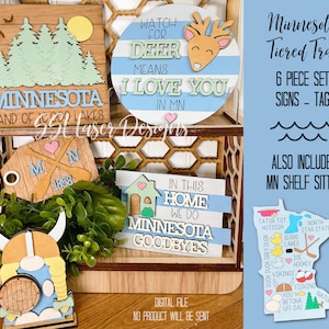 May include: A six-piece set of Minnesota-themed tiered tray signs, including a tag that says "Minnesota, Land of 10,000 Lakes", a sign that says "Watch for Deer, Means I Love You in MN", a sign that says "In This Home We Do Minnesota Goodbyes", a sign with a heart and the text "MN 1858", a Viking helmet, and a Minnesota state outline with various icons.