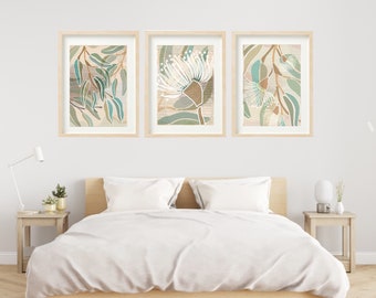 May include: Three framed prints of botanical illustrations featuring white flowers and green leaves on a beige background. The prints are hung on a white wall above a bed with white bedding.