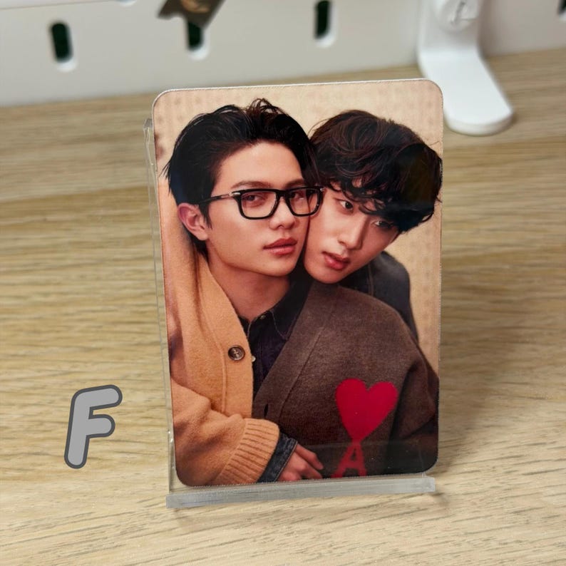May include: A photograph of two people embracing, displayed in a clear acrylic stand. One person wears glasses and a tan sweater, while the other is in a brown jacket. A red heart is visible on the jacket.