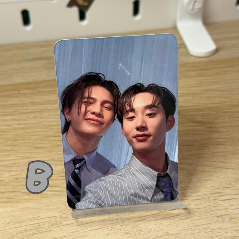 May include: A photo card featuring two men in collared shirts and ties, smiling at the camera. The card is propped up on a clear stand. The letter "B" is visible in the lower left corner.