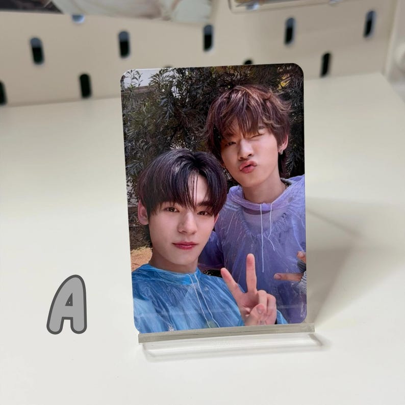 May include: A photograph of two young men, one in a blue shirt and the other in a purple hoodie. The photo is displayed in a clear acrylic stand. The letter "A" is visible in the lower left corner.
