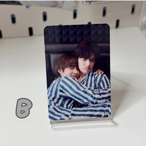 May include: A rectangular photo card featuring two people in striped pajamas embracing. The card is propped up on a clear acrylic stand. The letter "B" is visible in the lower left corner.