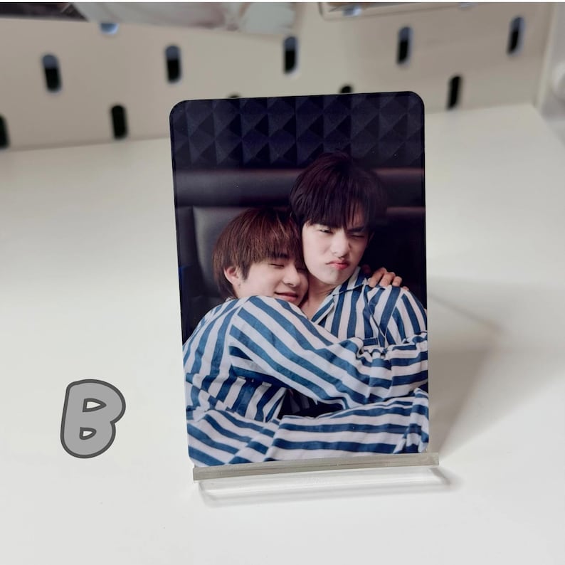 May include: A rectangular photo card featuring two people in striped pajamas embracing. The card is propped up on a clear acrylic stand. The letter "B" is visible in the lower left corner.