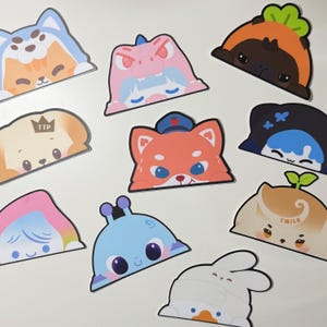 May include: A collection of nine colourful die-cut stickers featuring various cartoon characters, including animals in costumes, a blue alien, and figures with text like TTP and TMILK, all designed with a flat, graphic style and bold outlines.