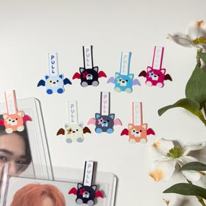 May include: A selection of colourful bat-shaped pull tabs, each printed with the word "PULL". The bats are in various colours, such as blue, black, pink, and orange, with matching wings. Some are attached to clear plastic sleeves.