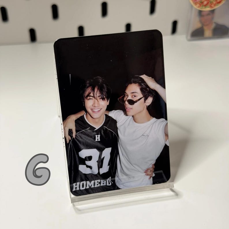May include: A clear acrylic photo stand holding a photograph of two young men. One man wears a black and white jersey with the number 31 and the word "HOMEBOY". The other man wears sunglasses and a white t-shirt.