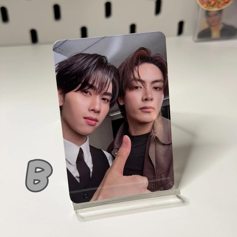 May include: A clear acrylic photo stand holding a photo of two young men. One man is wearing a black vest and tie, the other a brown jacket. The photo is a selfie with a thumbs-up gesture.