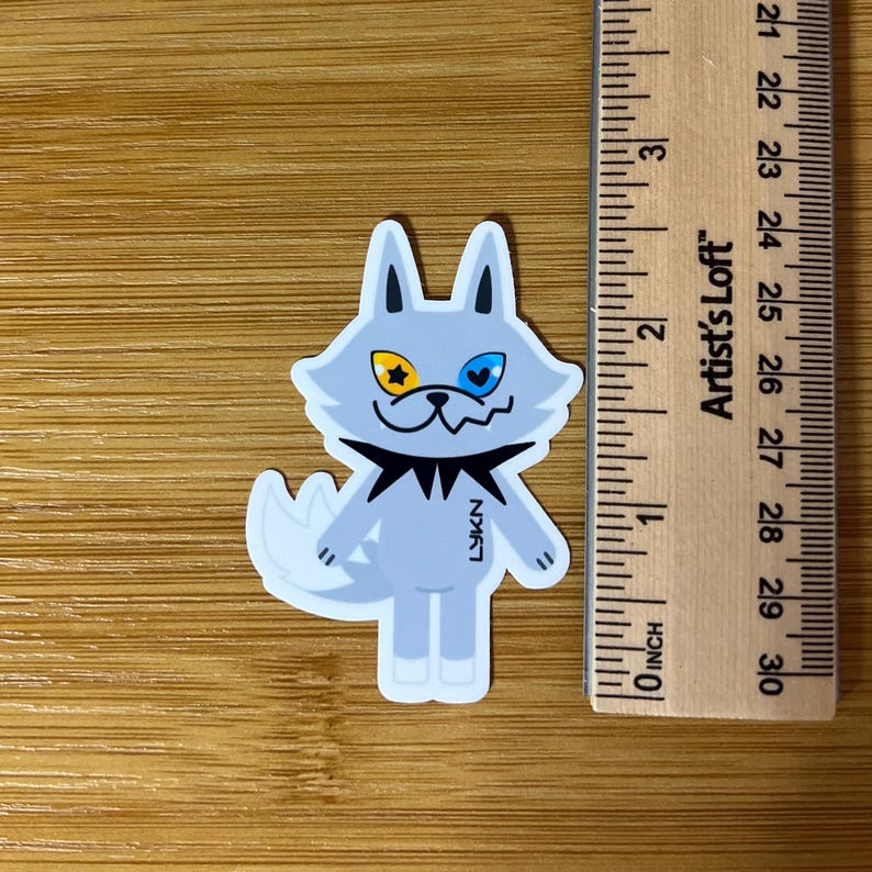 Op de afbeelding: Een sticker met een cartoonwolf met een lichtblauw lichaam, een zwarte kraag en een witte staart. De wolf heeft een geel ster-oog en een blauw hart-oog. De sticker is ongeveer 5 cm hoog.