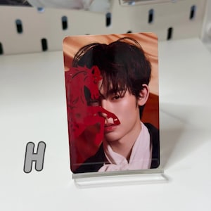 May include: A rectangular photo card featuring a person with dark hair and a red horse silhouette overlay. The card is displayed on a clear acrylic stand. The letter "H" is visible in the lower left corner.