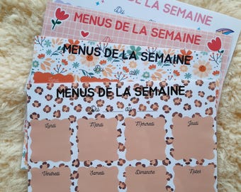 May include: A stack of weekly menu planners with various designs. The top planner has a disco ball graphic. Other planners feature floral, heart, and leopard print patterns. Each planner has the text "MENUS DE LA SEMAINE" and spaces for daily meal planning.