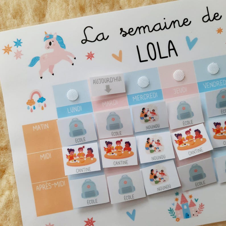 May include: A colorful weekly schedule chart for a child named Lola. The chart features a unicorn illustration, a rainbow, and various icons representing activities like school, daycare, and meals. The days of the week are labeled in French.