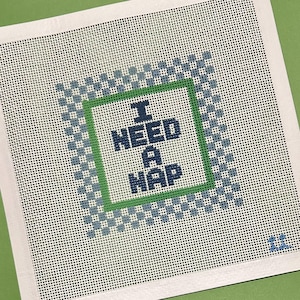 May include: A white canvas with a green and blue checkered border. Inside the border is a green square with the text "I NEED A NAP" in blue.