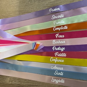 Peut inclure: Un ensemble de rubans en satin colorés avec des mots français imprimés dessus, notamment "Passion", "Sincérité", "Famille", "Complicité", "Force", "Bonheur", "Partage", "Fidélité", "Confiance", "Amour", "Santé", et "Longévité".