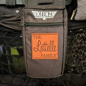 May include: A gray stroller organizer with a black zipper and a brown leather patch that says "THE Lattelle FAMILY". The organizer has a white logo that says "KEENZ" with a star.