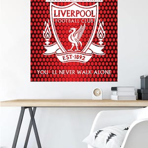 Puede incluir: Un póster rojo y negro con el escudo del Liverpool Football Club. El escudo es blanco y presenta un pájaro con una corona, un escudo y las palabras "You'll Never Walk Alone".