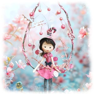 May include: A handmade doll in a pink dress and a striped hat, sitting in a decorative floral arch. The doll has black hair and is surrounded by pink blossoms and berries, creating a whimsical, fairy-tale aesthetic.