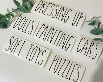 May include: Five white labels with black text, each with a different category for toys: "Dressing Up", "Dolls", "Painting Cars", "Soft Toys", and "Puzzles".
