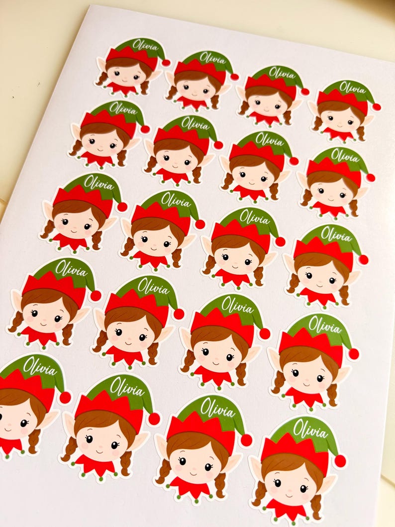 May include: A sheet of twenty-one die-cut stickers featuring a cartoon elf with brown hair in braids, wearing a red and green hat. Each sticker includes the name Olivia printed in white script on the green portion of the hat.