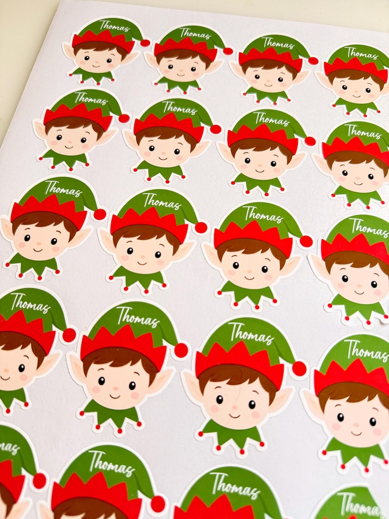 May include: A sheet of multiple circular stickers featuring a cartoon elf character with brown hair, pointed ears, and a green and red hat. Each hat displays the name Thomas in white cursive script. The stickers are arranged in a grid pattern.