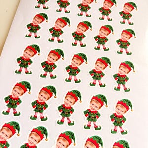 May include: A sheet of twenty-five identical stickers featuring a cartoon elf with a child's face. Each elf wears a green tunic, a green hat with a gold bell, and red and white striped leggings, standing with hands on hips.