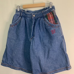 May include: Blue denim shorts with a high waist and a button closure. The shorts feature red stitching and a plaid pocket detail with the embroidered letters "BF". The shorts are hanging on a wooden hanger.