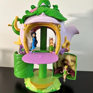 Peut inclure: Un ensemble de jeu de fête de thé de fées aux couleurs vert, violet et jaune. L'ensemble de jeu est en forme de théière et comprend une table et trois figurines de fées. Le design comprend des accents de feuilles et de fleurs.