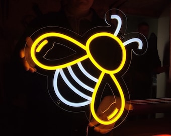 May include: A neon sign shaped like a bee with yellow and white outlines. The sign is being held by a person in a dark room.