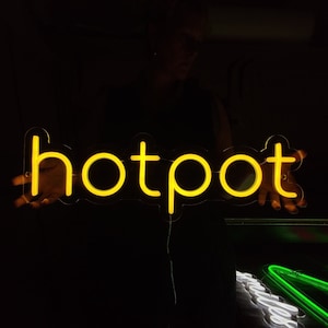 May include: A yellow neon sign that reads "hotpot" in a dark room.