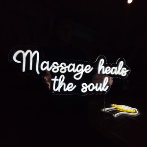 May include: White neon sign with the text "Massage heals the soul" in a cursive font.