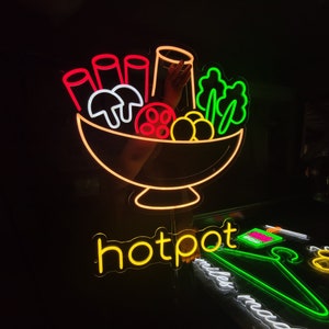 May include: Neon sign depicting a bowl of food, including mushrooms, noodles, and vegetables. The sign reads "hotpot" in yellow neon.