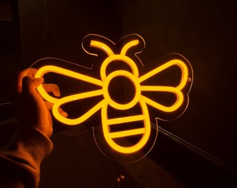 May include: A neon sign shaped like a bee, with a yellow glow. The bee has a round body and two wings.