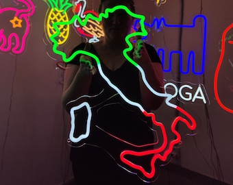 May include: A person stands in front of a wall with neon signs. The signs are in various shapes and colors, including a pineapple, a dog, a cowboy hat, and a map of Italy. The map of Italy is outlined in red, white, and green neon lights.