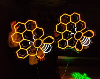 May include: Two neon signs shaped like honeycombs with bees inside. The signs are lit up in a warm orange color.
