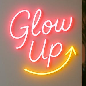 May include: A neon sign with the words "Glow Up" in a cursive font. The word "Glow" is in a bright red color, and "Up" is in white. A yellow arrow curves upward beneath the words, suggesting growth and improvement.