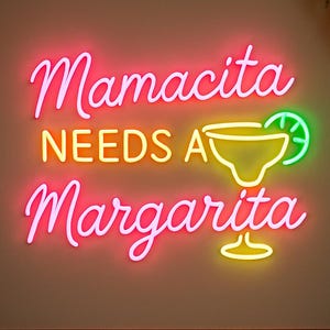 Puede incluir: Un letrero de neón con las palabras "Mamacita NEEDS A Margarita" en escritura cursiva rosa y amarilla. También se muestra un vaso de margarita de neón con una rodaja de lima. El letrero está montado en una pared de color neutro.