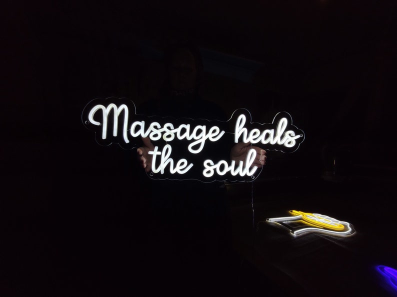 May include: White neon sign with the text "Massage heals the soul" on a black background.