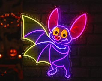 May include: A neon sign in the shape of a cartoon bat with yellow, purple, and pink lights. The bat has large ears, a smiling face, and outstretched wings. The sign is mounted on a dark brick wall, with Halloween decorations in the background.
