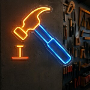 May include: Neon sign depicting a hammer and nail. The hammer is outlined in yellow and blue, with the nail in orange. The sign is mounted on a dark gray wall, with tools visible in the background.
