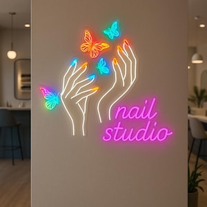 May include: Neon sign for a nail studio. It features white hands with colourful nails, butterflies, and the words "nail studio" in pink. The butterflies are in vibrant colours, including orange, blue, and green.